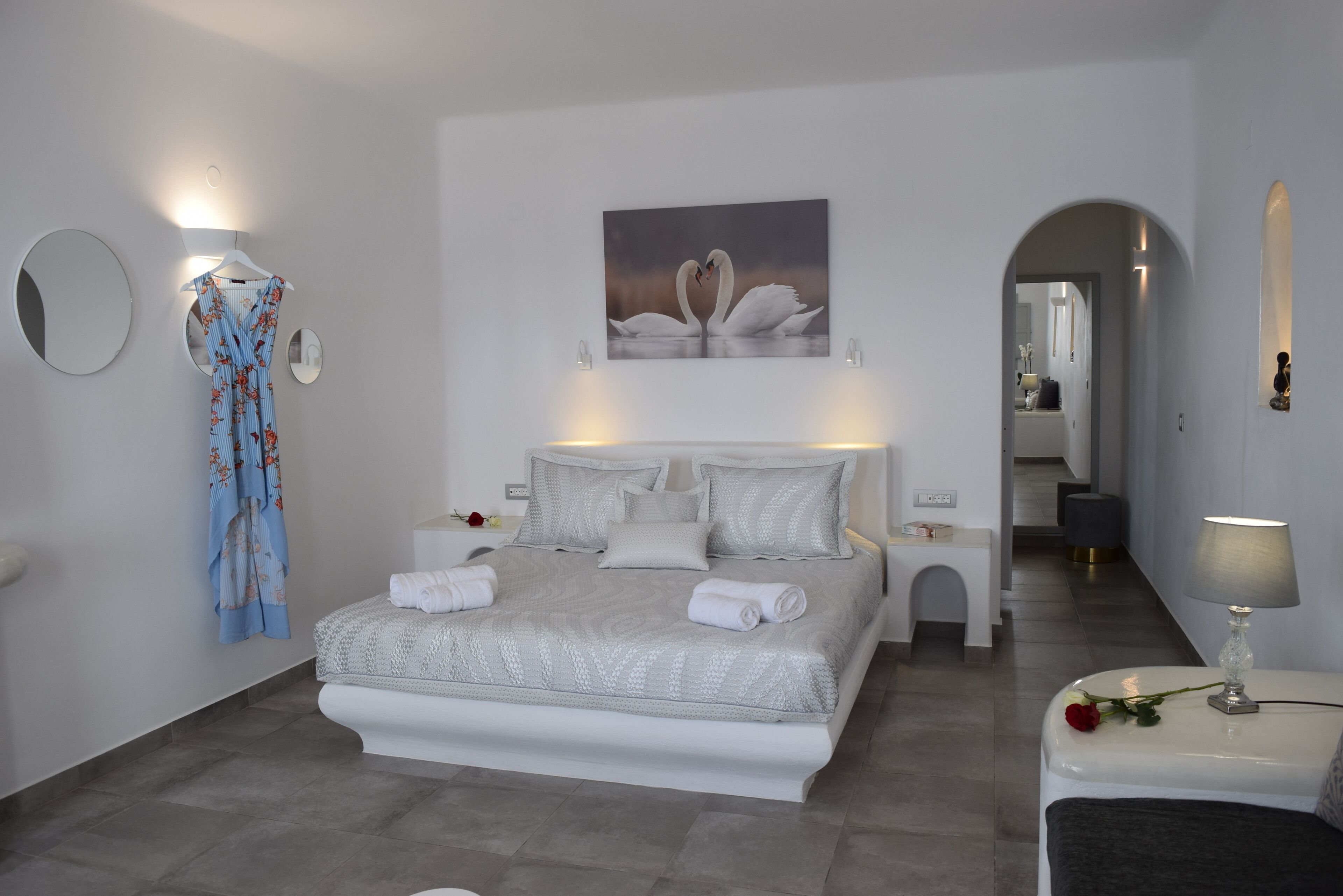 A modern bedroom with a large bed, a nightstand, a bedside table, and a wall-mounted mirror.
