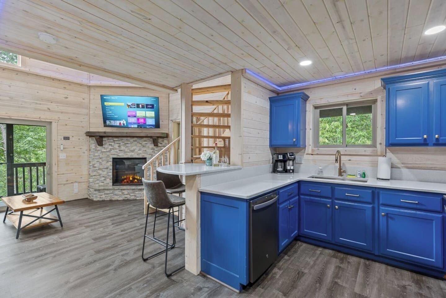 A modern kitchen with blue cabinets, a stone fireplace, and a bar area.