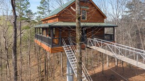 Une cabane en bois avec un toit vert, un balcon et un pont de corde.