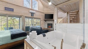 A wooden cabin interior with a bed, a seating area, a fireplace, and a large bathtub. - Top of the Line Treehouse Cabin (Cleveland)