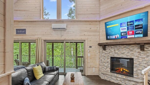 A cozy room with a stone fireplace, a leather sofa, and a large TV displaying streaming services. - Top of the Line Treehouse Cabin (Cleveland)