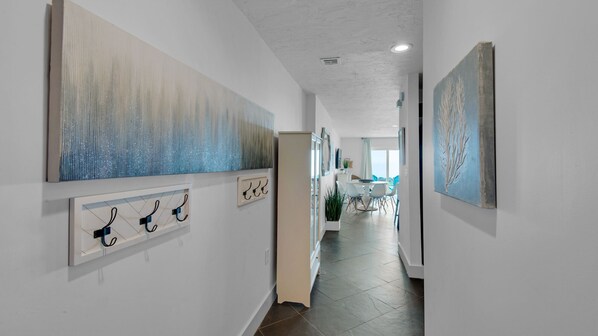 A hallway with artwork on the walls, a coat rack, and a dining area in the distance.