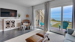 Un salon avec un téléviseur, un fauteuil en osier, un canapé et une vue sur la mer.