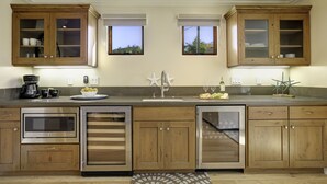 Una cocina moderna con gabinetes de madera, electrodomésticos de acero inoxidable y dos ventanas con persianas.