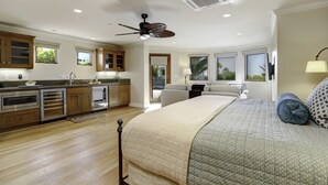Un dormitorio amplio con una cama grande, un ventilador de techo y vistas al exterior a través de las ventanas.