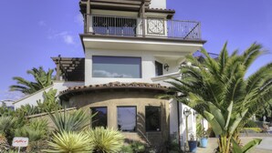 Una casa de varios pisos con balcón, ventanas grandes y un jardín con diversas plantas.