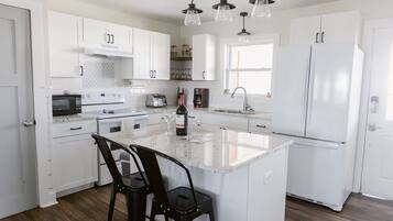 A modern kitchen with white cabinetry, a central island, bar stools, a wine bottle, and a built-in oven.