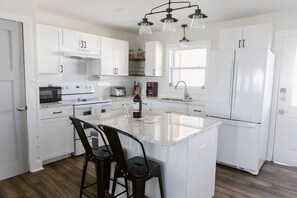 Una cocina moderna con armarios blancos, una isla central, taburetes de bar, una botella de vino y un horno empotrado.