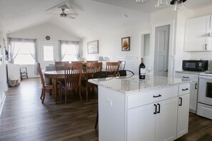 Una cocina moderna con armarios blancos, un comedor con sillas de madera, una isla central y un ventilador de techo.