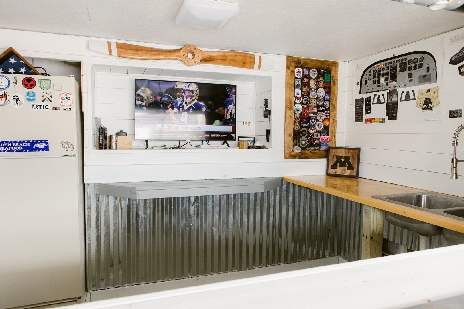 A kitchen with a TV mounted above a counter, a wooden accent wall, and various wall decorations.