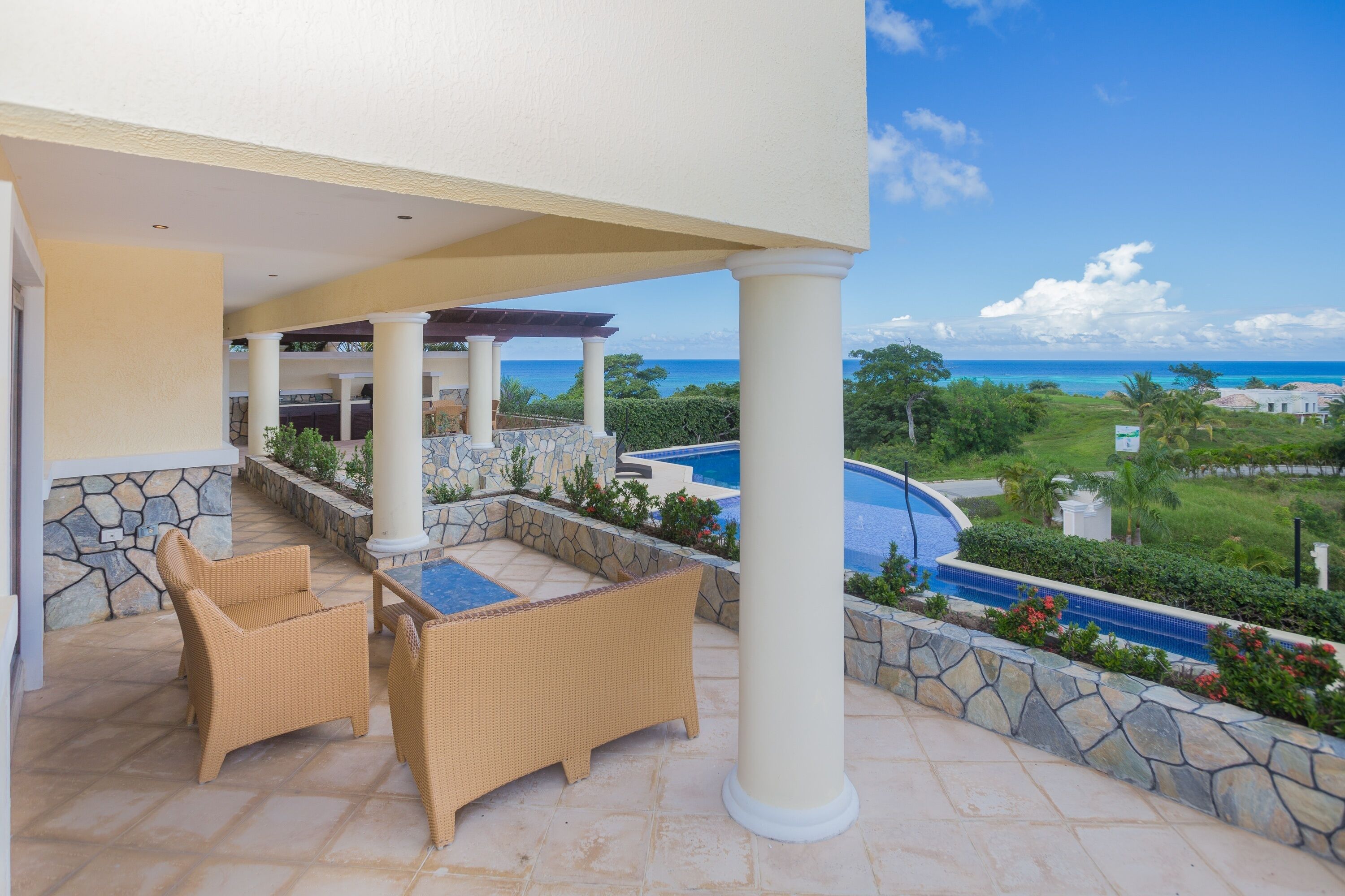 A covered outdoor area with wicker furniture, a stone pool, and a view of the ocean.
