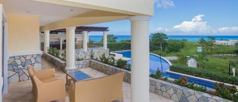 A covered outdoor area with wicker furniture, a stone pool, and a view of the ocean.