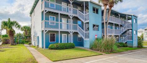 A multi-story building with balconies, a parking lot, and a well-maintained lawn.