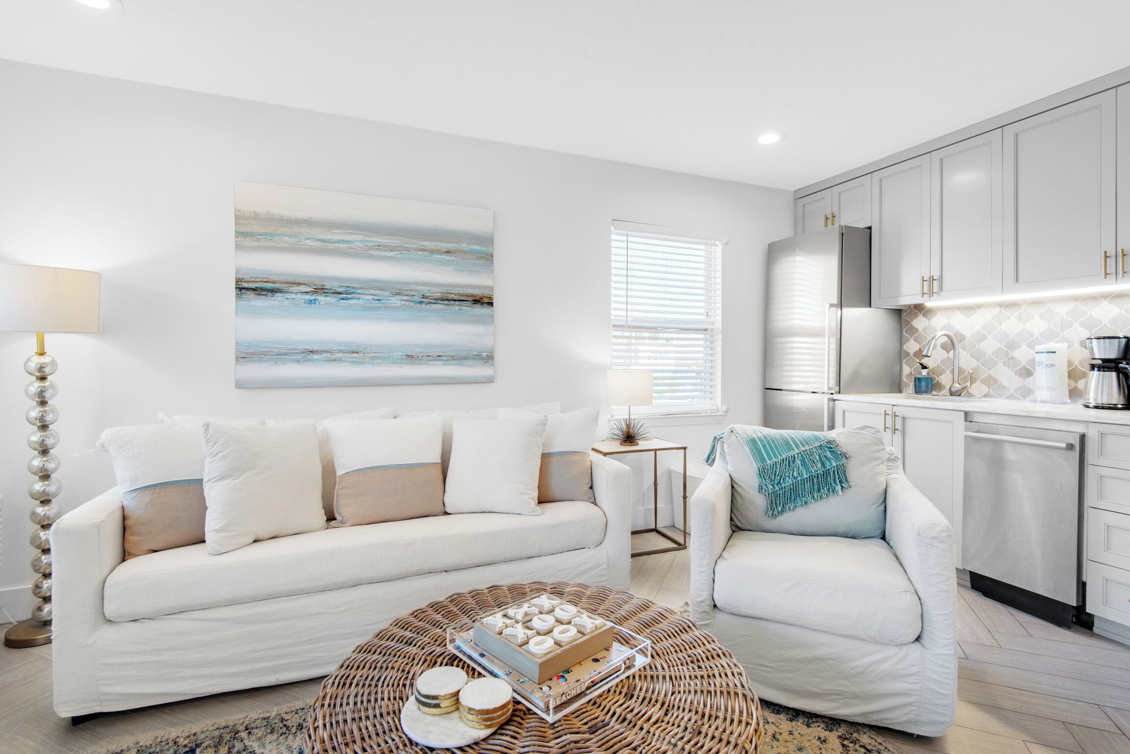 A modern living room with a white sofa, a coffee table with a decorative box, and a kitchen area with white cabinets and a refrigerator.