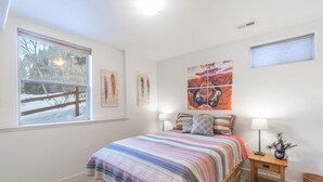 Ein Schlafzimmer mit einem Bett, zwei Nachttischen, einem Fenster und Kunstwerken an den Wänden.