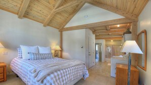 Een slaapkamer met een groot bed, houten balken in het plafond, een nachtkastje en een lamp.
