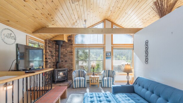 A cozy room with a wooden ceiling, a brick fireplace, a television, striped chairs, and a blue sofa. - Cozy Loft Located in the Heart of Ouray | Air Conditioning! (Ouray)