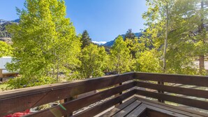 A wooden bench with a view of a forested area and mountains in the background. - Cozy Loft Located in the Heart of Ouray | Air Conditioning! (Ouray)