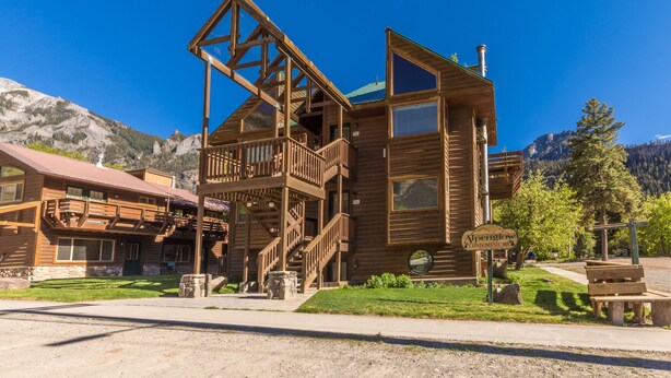 A wooden lodge with a balcony and a mountain backdrop.