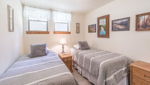 A bedroom with two single beds, a nightstand with a lamp, and three framed pictures on the wall.