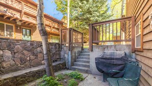 A wooden cabin with a stone wall, a barbecue grill, and a metal bench.