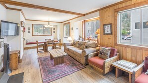 Ein gemütliches Wohnzimmer mit Holzboden, einer Couch, einem Esstisch und einem an der Wand befestigten Fernseher.