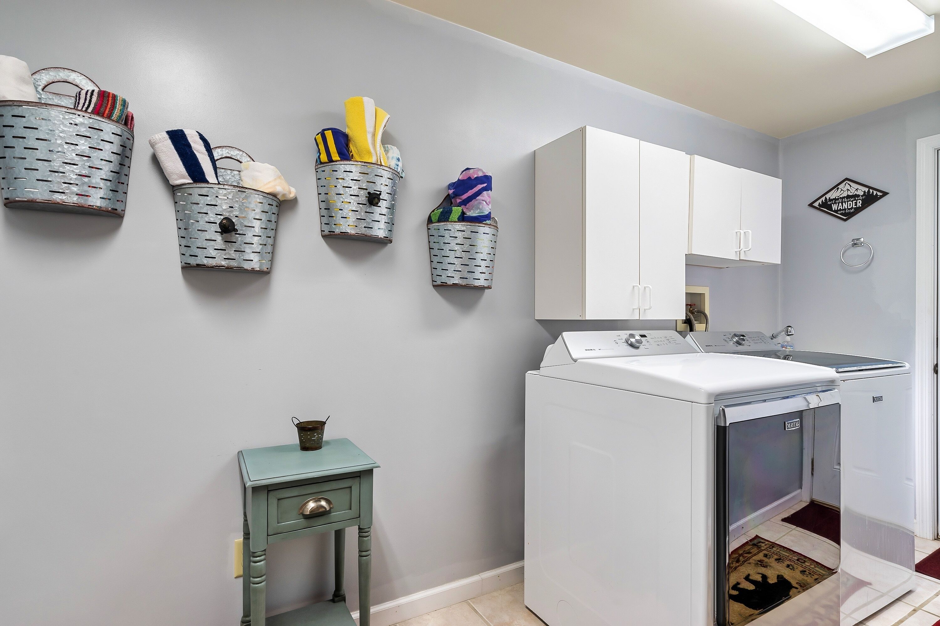 A laundry area with a washing machine, a dryer, and three wall-mounted baskets with towels and cloths.