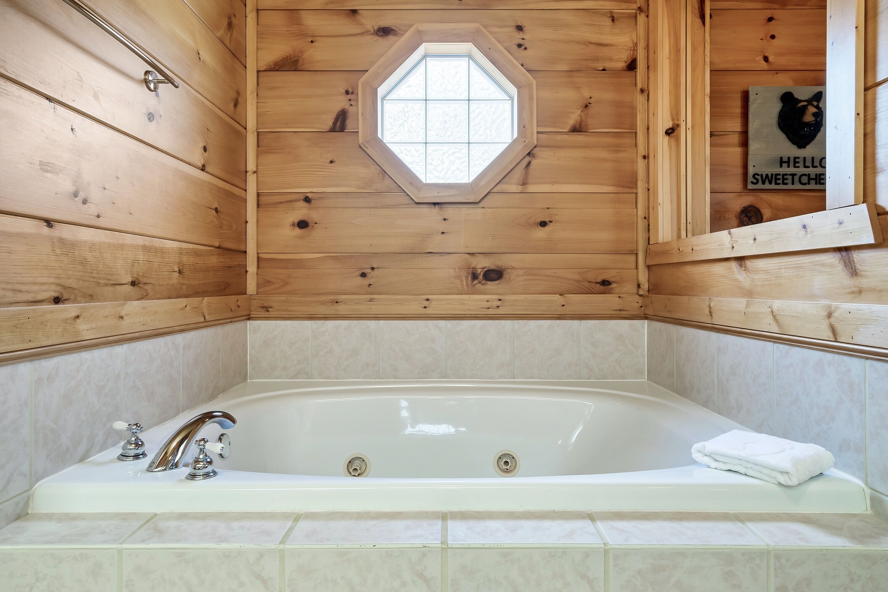 A wooden cabin bathroom with a bathtub, a wooden window, and a towel on the edge.