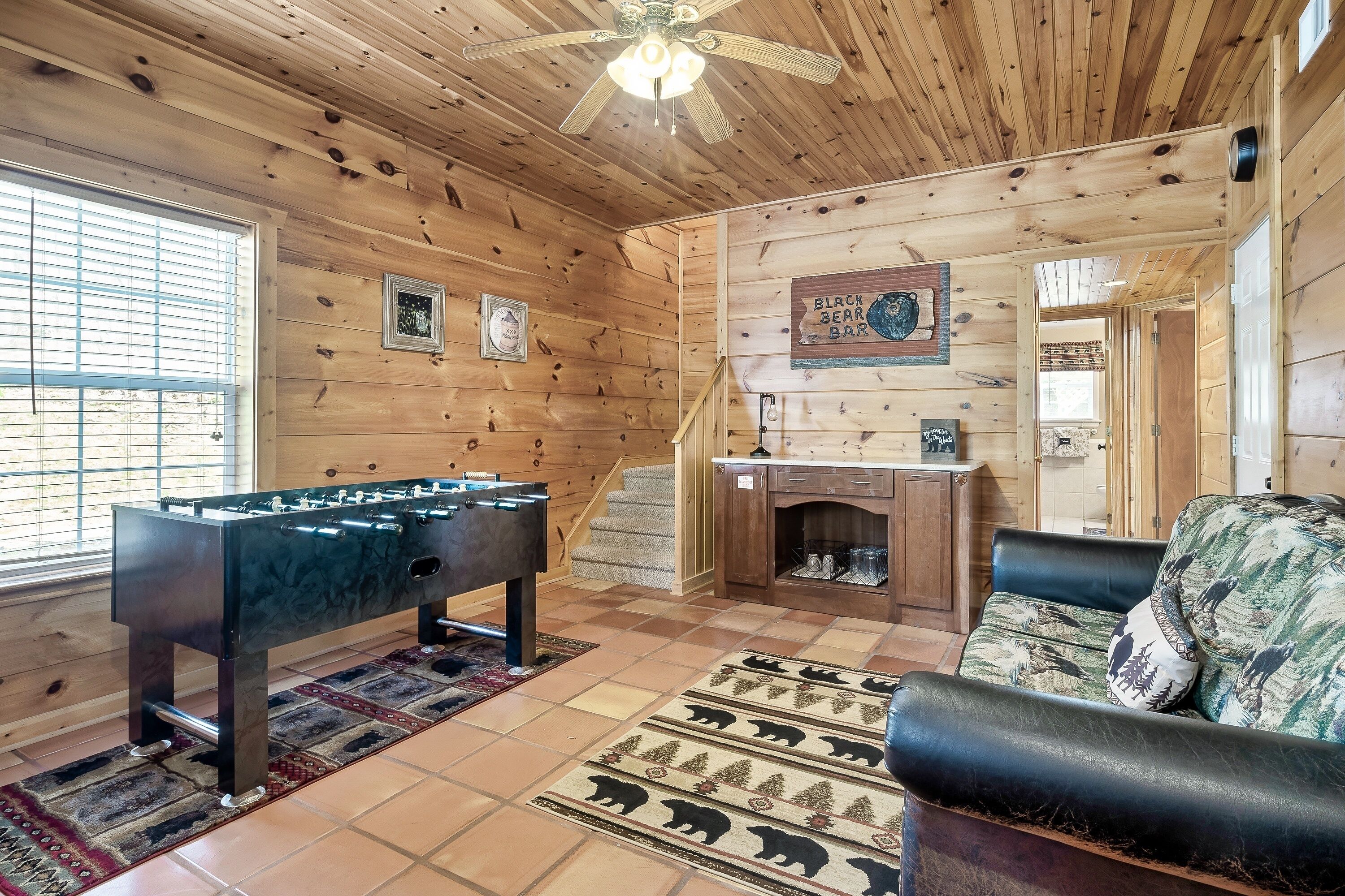 A cozy room with wooden walls, a foosball table, a sofa, and a fireplace.