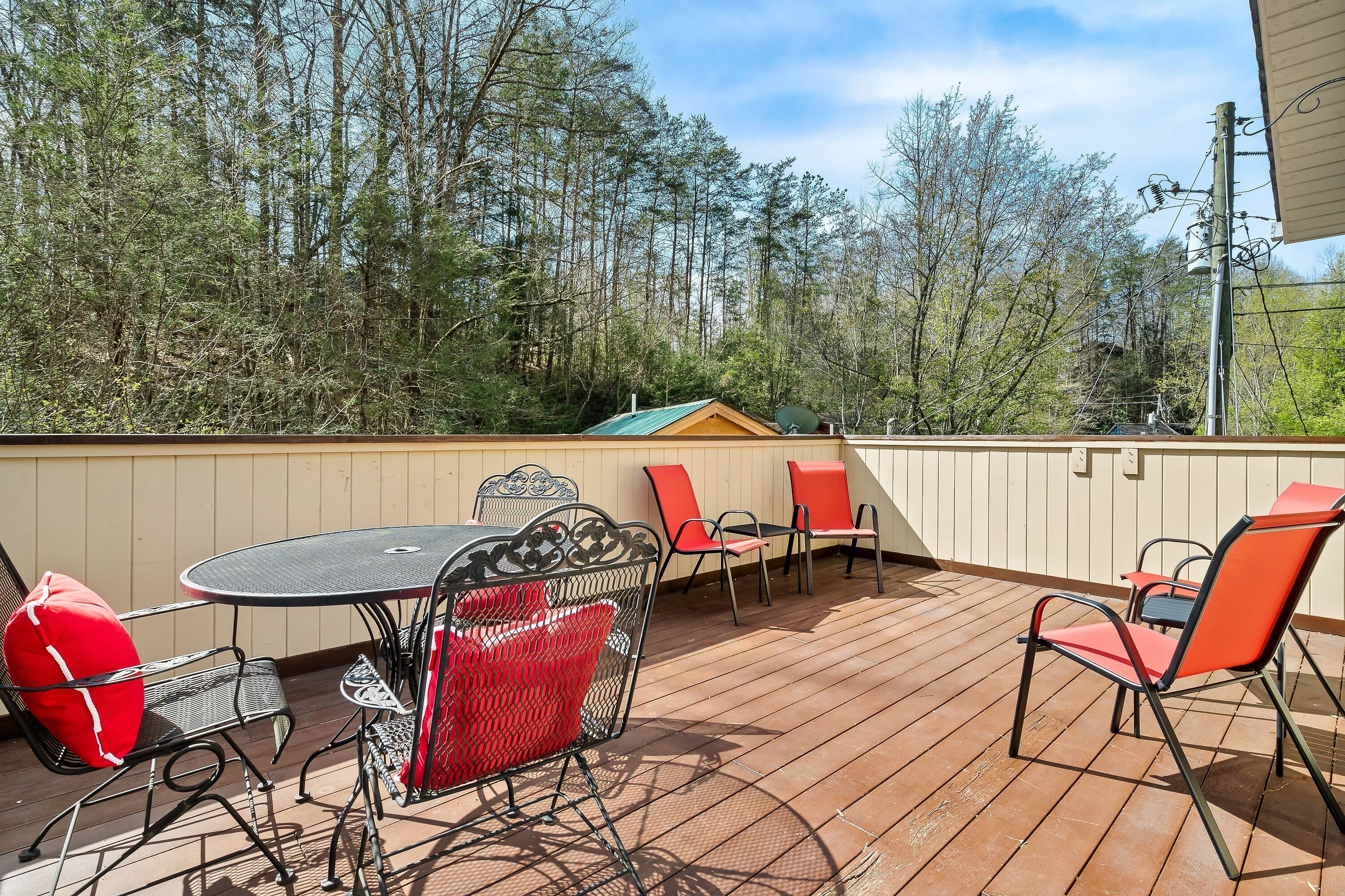 An outdoor patio with a round table and chairs, surrounded by a wooden deck and a view of trees.