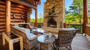 A log cabin with a stone fireplace, wicker furniture, and a wooden deck. - Legend- A Legendary Waterfront Stay in Ellijay, GA (Ellijay)
