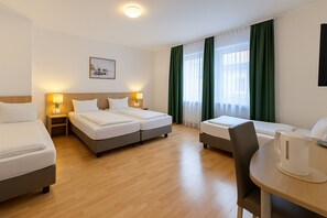 Habitación de hotel con dos camas, un escritorio y una silla. Hay dos mesitas de noche con lámparas, una ventana con cortinas verdes y un cuadro en la pared.