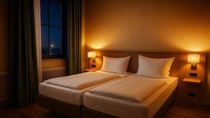 Una cama doble con dos mesitas de noche, cada una con una lámpara de pared, en una habitación con vista a la ciudad de noche.