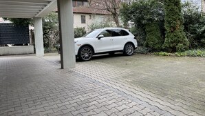 Un SUV blanco estacionado bajo un techo, con un camino de entrada pavimentado.