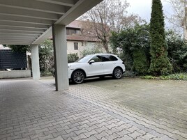 Un SUV blanco estacionado bajo un techo, con un camino de entrada pavimentado.