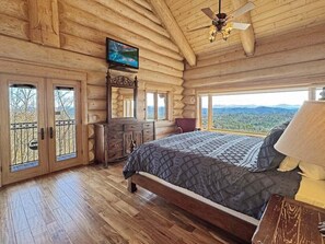 Ein Schlafzimmer in einer Blockhütte mit Bett, Kommode, Fernseher und einem Balkon mit Blick.