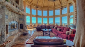Amplia sala de estar con chimenea de piedra, ventanas grandes y vistas a las montañas.
