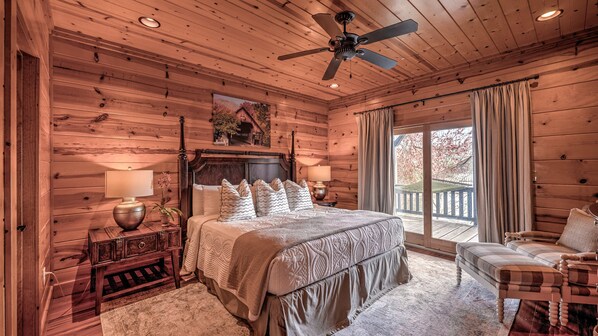A cozy log cabin bedroom with a large bed, wooden headboard, and a ceiling fan.
