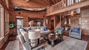 A spacious living area with a high ceiling, wooden walls, and a staircase leading to an upper level.