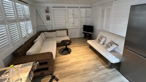 A compact living space with a sofa, a small table, a television, and a refrigerator. - Résidence Aigue Marine Sainte Anne - Maison Corail (Sainte-Anne)