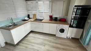 A compact kitchen with a sink, washing machine, and a built-in oven. - Résidence Aigue Marine Sainte Anne - Maison Corail (Sainte-Anne)