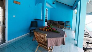 Uma área de refeições com uma mesa posta para dois, rodeada por cadeiras de madeira e um sofá. Uma placa na parede diz "Jade".