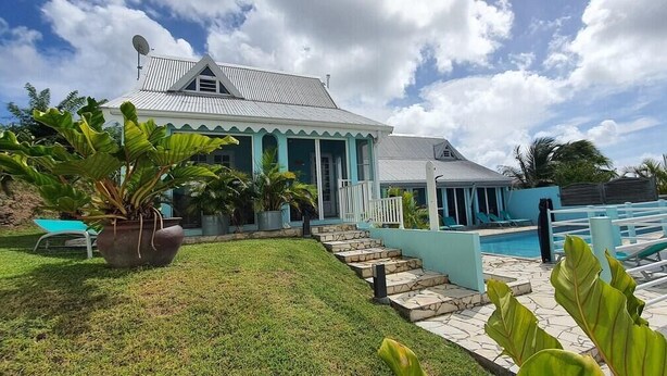 Uma casa com piscina, varanda coberta e gramado com plantas tropicais.