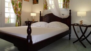Quarto com cama de dossel, duas mesas de cabeceira com abajures, cortinas florais e uma janela com vista.