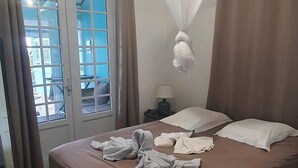 Ein Hotelzimmer mit Bett, Nachttisch, Lampe, einem Fenster mit Vorhängen und Blick nach draußen.