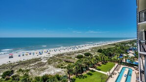 A beach view from a balcony with a pool and umbrellas. - 🌴🌞Lazy River + Indoor/Outdoor Pools | Oceanfront | South Wind 801 (Myrtle Beach)