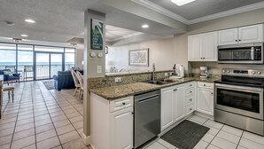 A modern kitchen with white cabinets, stainless steel appliances, and a large window overlooking the ocean. - 🌴🌞Lazy River + Indoor/Outdoor Pools | Oceanfront | South Wind 801 (Myrtle Beach)