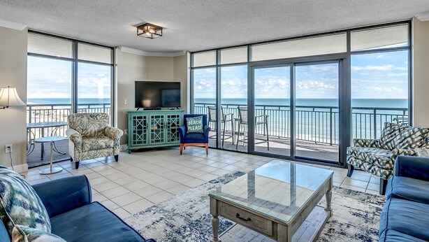 A spacious living area with a large glass door leading to a balcony with a view of the ocean. There are two sofas, a coffee table, and a television on a cabinet. - 🌴🌞Lazy River + Indoor/Outdoor Pools | Oceanfront | South Wind 801 (Myrtle Beach)