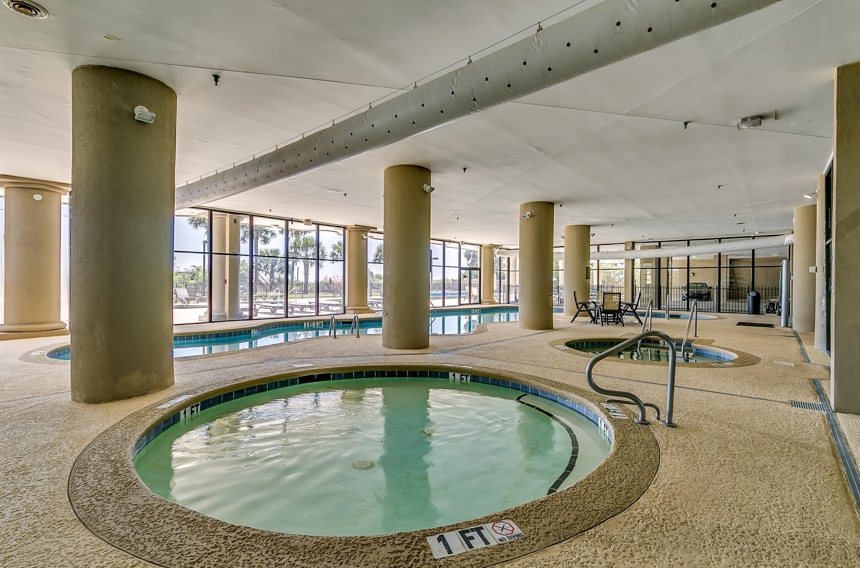 An indoor swimming pool with clear water, surrounded by beige pillars and a tiled floor.