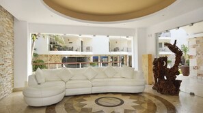 A modern interior with a white leather sofa, a decorative wooden sculpture, and a view of the building's exterior. - Beautiful oceanfront apartment, 1 block from 5th Av. (Playa del Carmen)